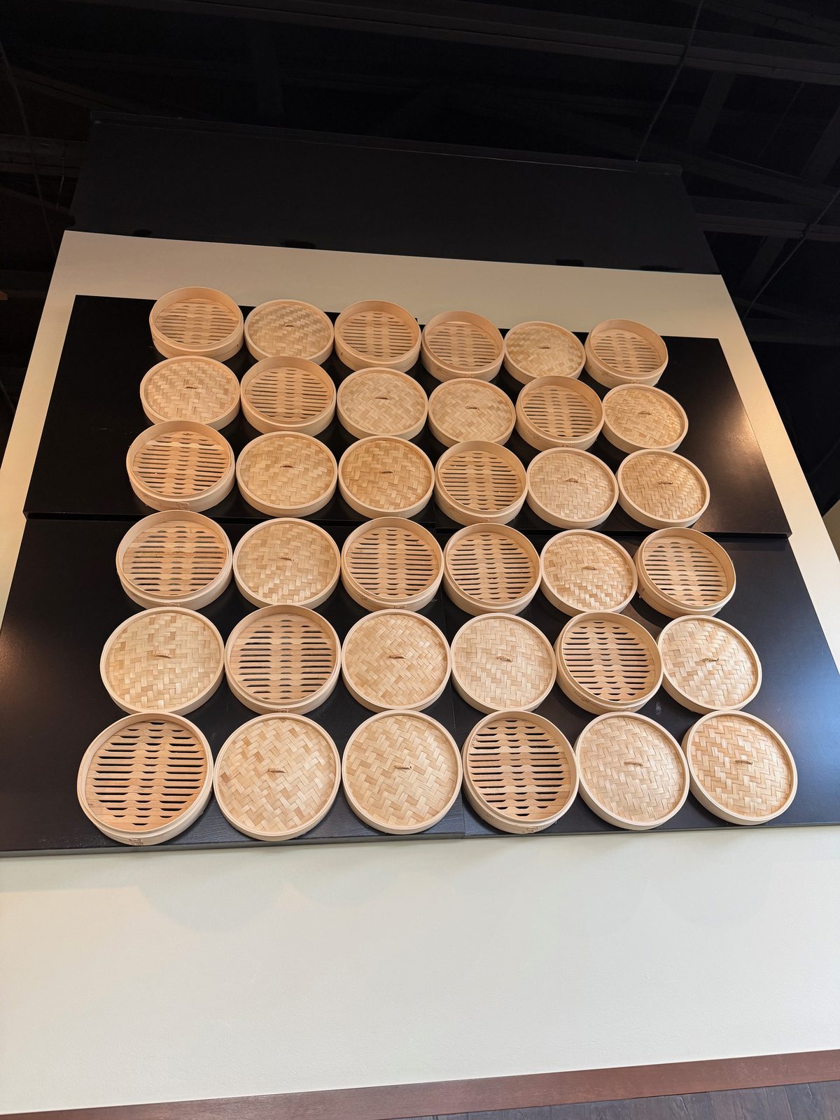 A wall entirely covered in stacked bamboo steamer baskets at Dough Zone, dozens of them arranged in rows as decor