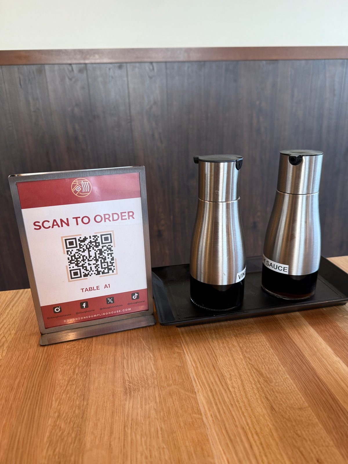 A table setting at Dough Zone with a Scan To Order QR code sign for Table A1 next to stainless steel vinegar and soy sauce dispensers